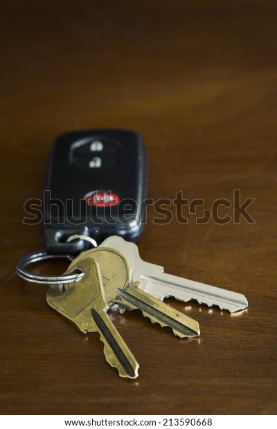 A close-up shot of a remote key\
fob or an automobile and three metal door keys on a key\
ring.