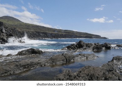 A close-up shot of a rocky coastline on São Miguel, Azores, where the ocean waves crash violently against the rocks. The scene captures the rugged terrain and powerful surf in a dramatic display - Powered by Shutterstock