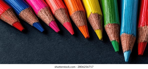 A close-up shot of a row of sharpened colored pencils in various bright hues, arranged diagonally on a dark, textured background.
