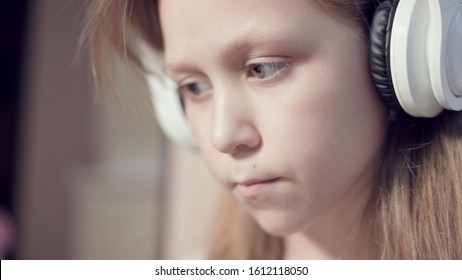 A close-up shot of a rushing plan portrait of a serious pensive and detached girl who is 10 years old in large white headphones indoors. Side look - Shutterstock ID 1612118050