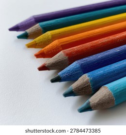 A close-up shot of several sharpened colored pencils arranged diagonally on a plain white surface, showcasing a spectrum of vibrant colors.