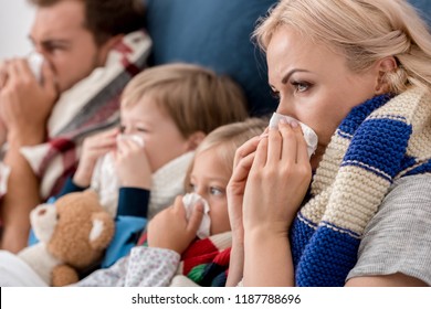 Close-up Shot Of Sick Young Family Blowing Noses With Napkins Together While Lying In Bed