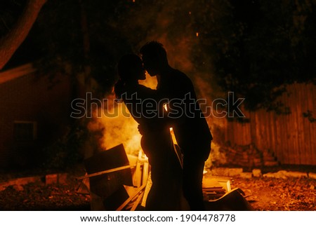A closeup shot of silhouettes of a couple in front of a camp fire, holfing and hugging each other
