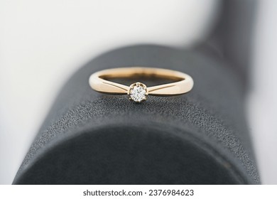 Close-up shot of a sleek gold ring showcasing a solitary diamond, positioned on a textured dark surface with a gentle white gradient background.