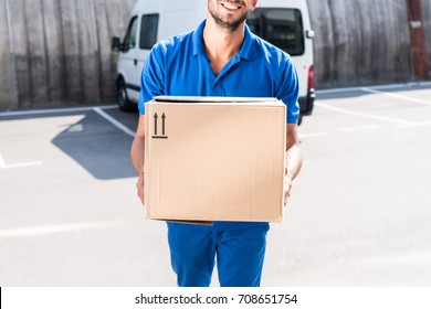 close-up shot of smiling delivery man carrying cardboard box