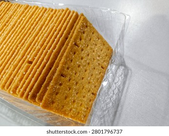 A close-up shot of a stack of golden brown crispy crackers sprinkled with sugar crystals inside a clear plastic tray packaging