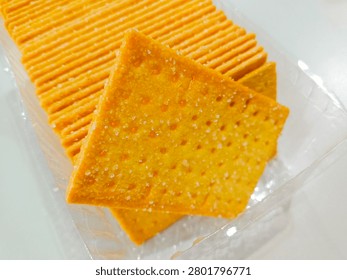 A close-up shot of a stack of golden brown crispy crackers sprinkled with sugar crystals inside a clear plastic tray packaging