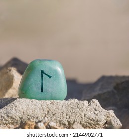 Close-up shot of a stone, especially a teal colored aventurine engraved with a Viking rune, especially the letter Laguz