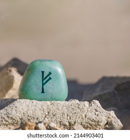 Close-up shot of a stone, especially a teal colored aventurine engraved with a Viking rune, especially the letter Fehu