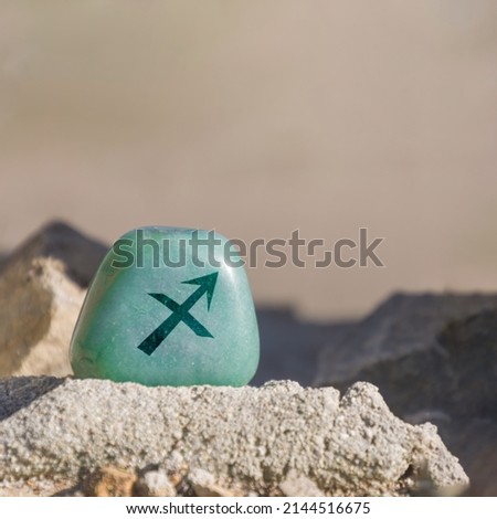 Close-up shot of a stone specifically a teal-colored aventurine engraved with a zodiac sign, in particular the sign of Sagittarius