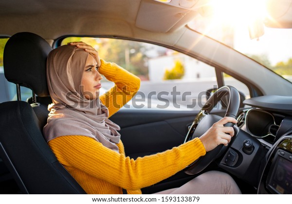 Closeup shot of stressed young\
Muslim woman driver in a car. Angry and tense Muslim woman stuck in\
the traffic.  Stressed woman driver sitting inside her\
car