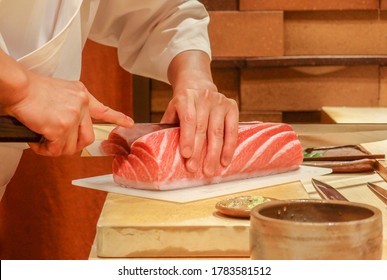 A close-up shot of a sushi chef cutting a chunk of fatty tuna on a cutting board at a high class sushi restaurant in Ginza, Tokyo, Japan.