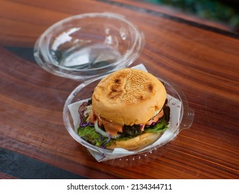 Closeup shot of take away delicious tasty yummy homemade juicy patty grilled beef cheeseburger with vegetable and melting thousand island sauce in disposable plastic round box package on wood table.