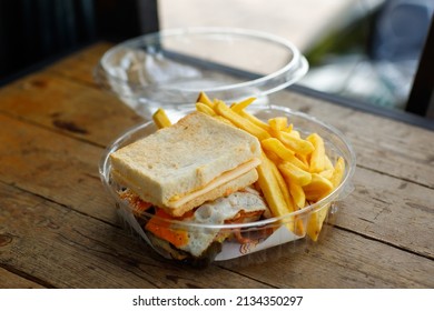 Closeup shot take away delicious tasty yummy homemade fried egg bacon and cheese sandwich with straight cut fresh frying french fries appetizer in disposable plastic round box package on wood table.