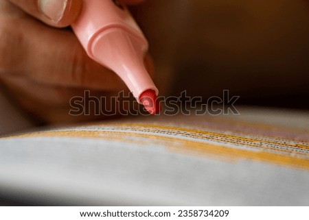 A closeup shot of taking notes with a pink highlighter pen with the blurred background