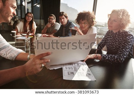 Closeup shot of team of young people going over paperwork. Creative people meeting at restaurant table. Focus on hands and documents.