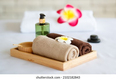 Closeup shot of Thai massaging stuffs herbal towel compress ball, coconut oil, perfume, cosmetics and plumeria flower in wooden tray placing on massage bed in spa therapy preparing for customer.