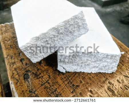 A close-up shot of two rectangular blocks of white styrofoam or expanded polystyrene (EPS) foam, stacked and resting on a rustic, glossy, dark brown wooden surface.