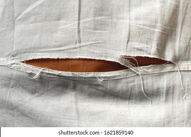 Close-up shot of unbleached beige fabric with torn stitch, hole and loose threads. Background of shabby worn cotton or linen material