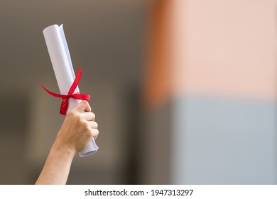 Close-up shot of a university graduate holding a degree certification to shows and celebrate education success on the college commencement day with sunlight in the background. - Shutterstock ID 1947313297