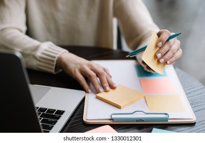 Closeup shot of university student hand holding pen, sticky note on planning board, exam preparation, learning language. Woman working start up project at workplace using scrum for productivity