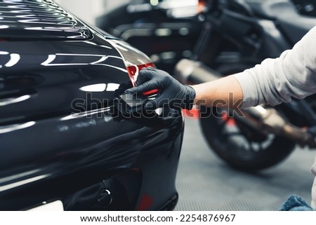 Close-up shot of unrecognisable man wearing black gloves applying ceramic coating to car using sponge. Professional car detailing. Horizontal indoor shot. High quality photo