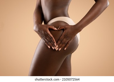 Closeup shot of unrecognizable black lady in beige underwear holding palms in heart-shaped symbol on her hips, well-fit african american woman using anti-cellulite beauty product, beige background