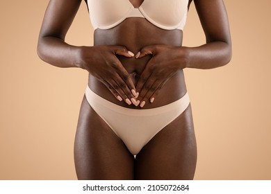 Closeup Shot Of Unrecognizable Black Lady In Beige Underwear Holding Palms In Heart-shaped Symbol On Her Belly, Beige Studio Background, Cropped, Gynecology And Womens Health Concept