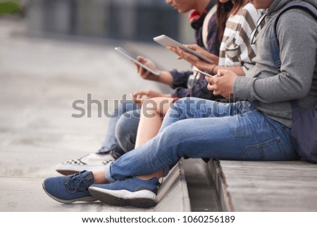 Close-up shot of unrecognizable friends gathered together outdoors and browsing Internet with help of devices, blurred background