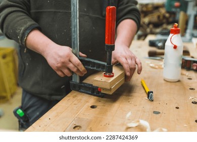 Closeup shot of unrecognizable male carpenter using bar clamp to glue two wood pieces together. Blue collar job. High quality photo - Powered by Shutterstock