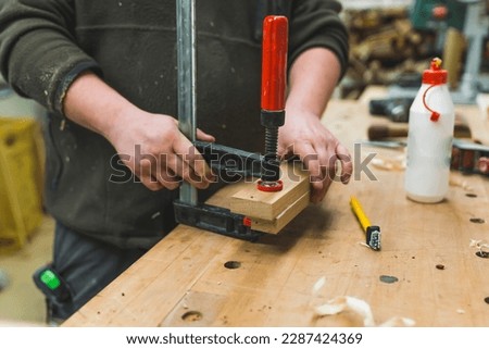 Closeup shot of unrecognizable male carpenter using bar clamp to glue two wood pieces together. Blue collar job. High quality photo