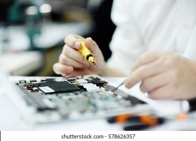 Closeup shot of unrecognizable man assembling circuit board using screwdriver and different tools on table in workshop