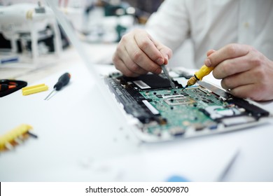 Closeup shot of unrecognizable man fixing circuit board in laptop using screwdriver and different tools on table in workshop - Powered by Shutterstock - Get 15% off with code: PIKWIZARD15