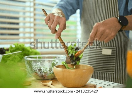 Closeup shot of unrecognizable senior man in apron making health vegetarian salad in kitchen
