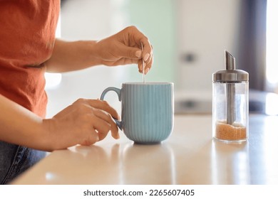 Closeup Shot Of Unrecognizable Woman Preparing Coffee In Kitchen, Young Female Holding Tea Spoon And Stirring Brown Sugar In Cup While Making Caffeine Drink In The Morning, Side View - Powered by Shutterstock