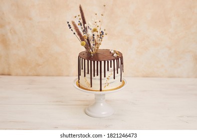 A Closeup Shot Of A Vanilla Cake With Chocolate Drip And Flowers On Top