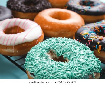 A close-up shot of a variety of donuts on a cooling rack. The donuts are topped with colorful sprinkles, pink stripes, and coconut flakes, with a focus on the front donut - Powered by Shutterstock