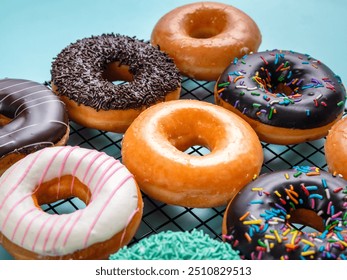 A close-up shot of a variety of donuts on a cooling rack. The donuts are topped with colorful sprinkles, pink stripes, and coconut flakes, with a focus on the front donut - Powered by Shutterstock