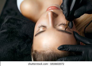 Closeup shot of a woman in black gloves applying permanent brow makeup to a young woman. Space for text