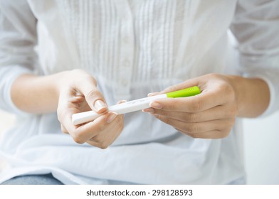 Closeup shot of a woman looking at pregnancy test. She's is checking her pregnancy exam. Detail hands of a girl holding pregnancy test. Shallow depth of field with focus on pregnancy test.