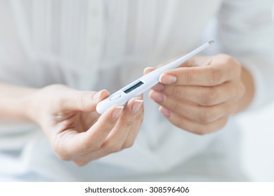 Closeup shot of a woman looking at thermometer. Female hands holding a digital thermometer. Girl measures the temperature. Shallow depth of field with focus on thermometer. - Shutterstock ID 308596406