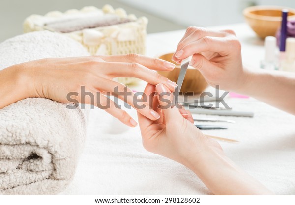Closeup shot of a woman in a\
nail salon receiving a manicure by a beautician with nail file.\
Woman getting nail manicure. Beautician file nails to a\
customer.
