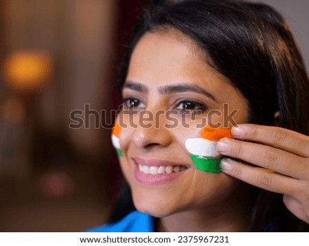 Closeup shot of a woman painting Tiranga on her face with a wide smile -patriotism, cricket fan, sports fan, Indian fan, support for India. Indian female with a proud gesture - India, Republic Day