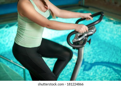 Closeup shot of woman riding exercise bike against swimming pool