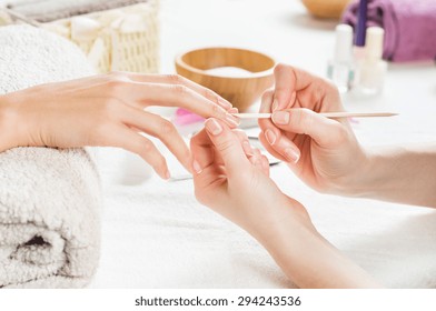 Closeup shot of a woman using a cuticle pusher to give a nail manicure. Nail technician giving customer a manicure at nail salon. Young caucasian woman receiving a french manicure. - Powered by Shutterstock