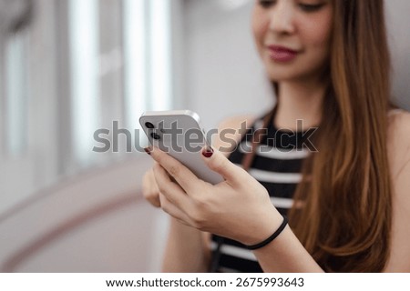 A close-up shot of a woman's hands using a smartphone while she travels on a sky train.