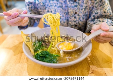 Close-up shot of women hands eating noodle with beef and poached egg. Delicious, looks very tasty