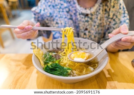 Close-up shot of women hands eating noodle with beef and poached egg. Delicious, looks very tasty