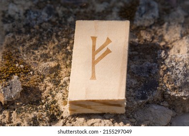 Close-up shot of a wooden tile engraved with a letter of the runic alphabet, especially the letter Fehu