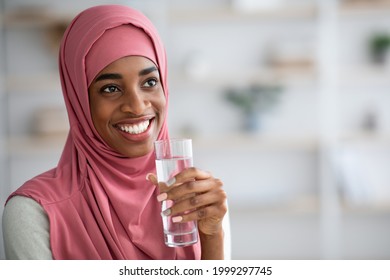 Closeup Shot Of Young Black Woman In Hijab Drinking Mineral Water From Glass At Home, Positive Smiling Islamic Lady Enjoying Healthy Refreshing Drink, Taking Care About Body Hydration, Free Space - Powered by Shutterstock